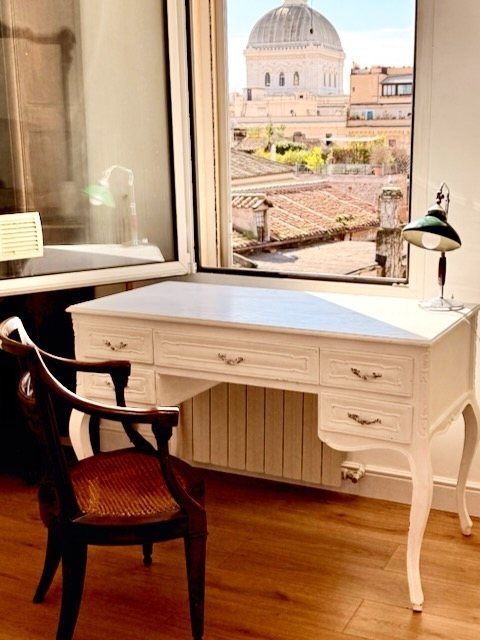 A desk by the open window of the apartment, with the dome of the Great Synagogue in the view