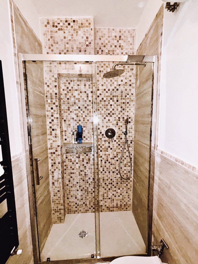 The shower, with a rain showerhead, mosaic tiles and a sliding glass door