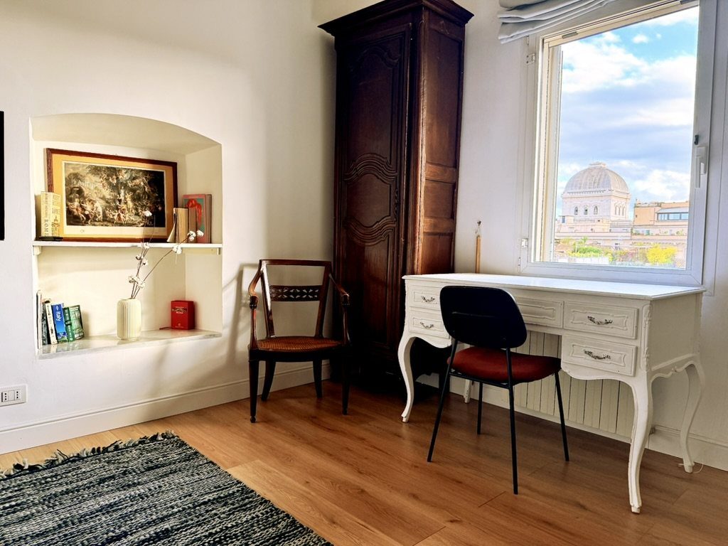 A corner of the apartment, with a white desk by the window and the dome of the Great Synagogue in view