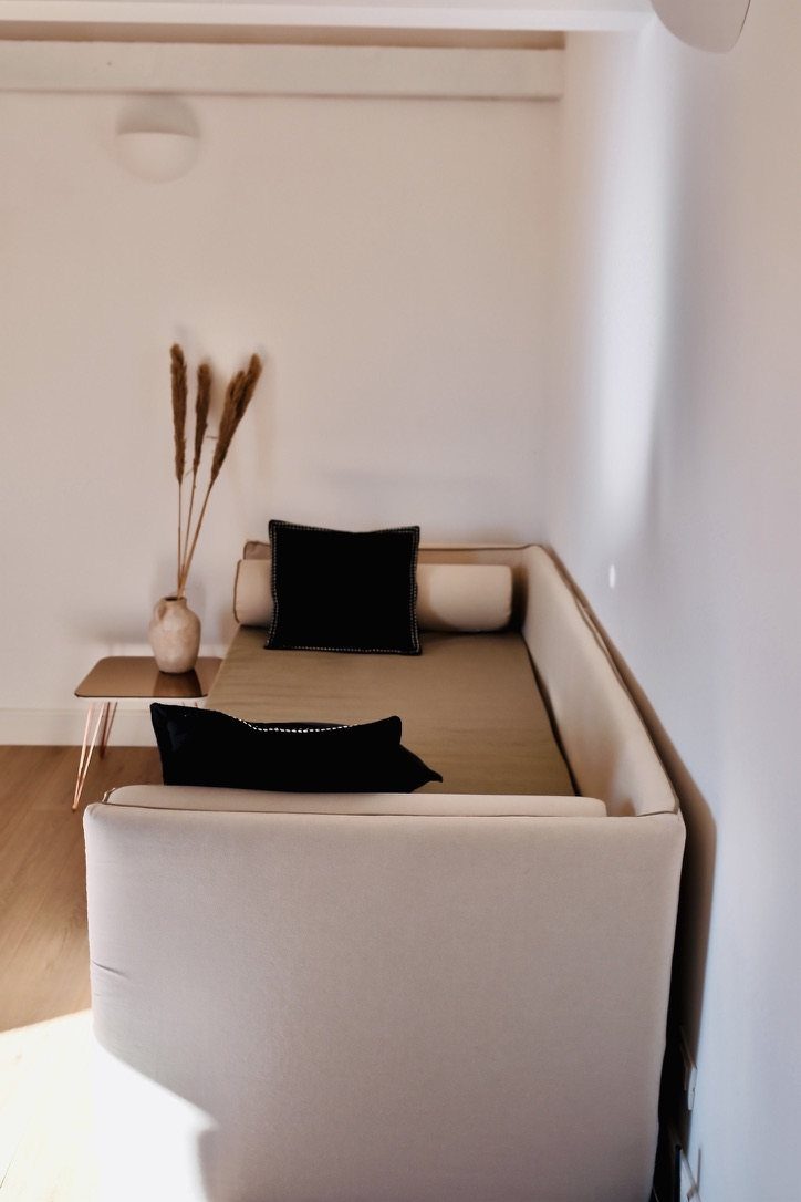 The sofa bed in the living room, with black cushions and a vase of dried grasses