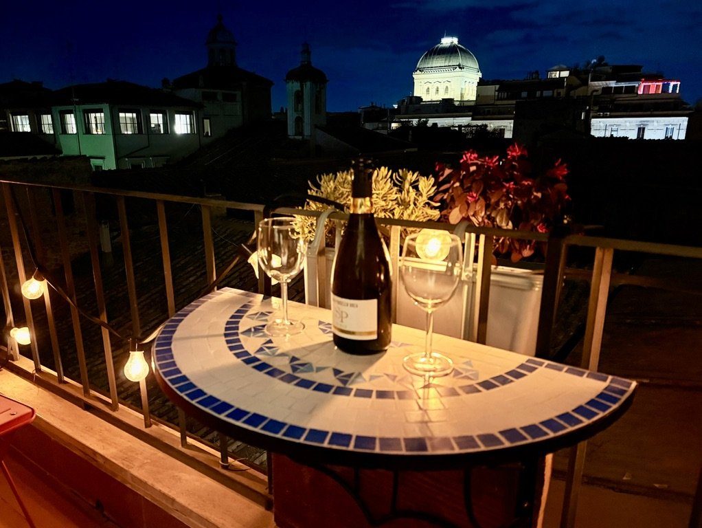 Evening on the balcony: a bottle of wine and two glasses on the mosaic table, with the dome of the Great Synagogue lit up behind the rooftops