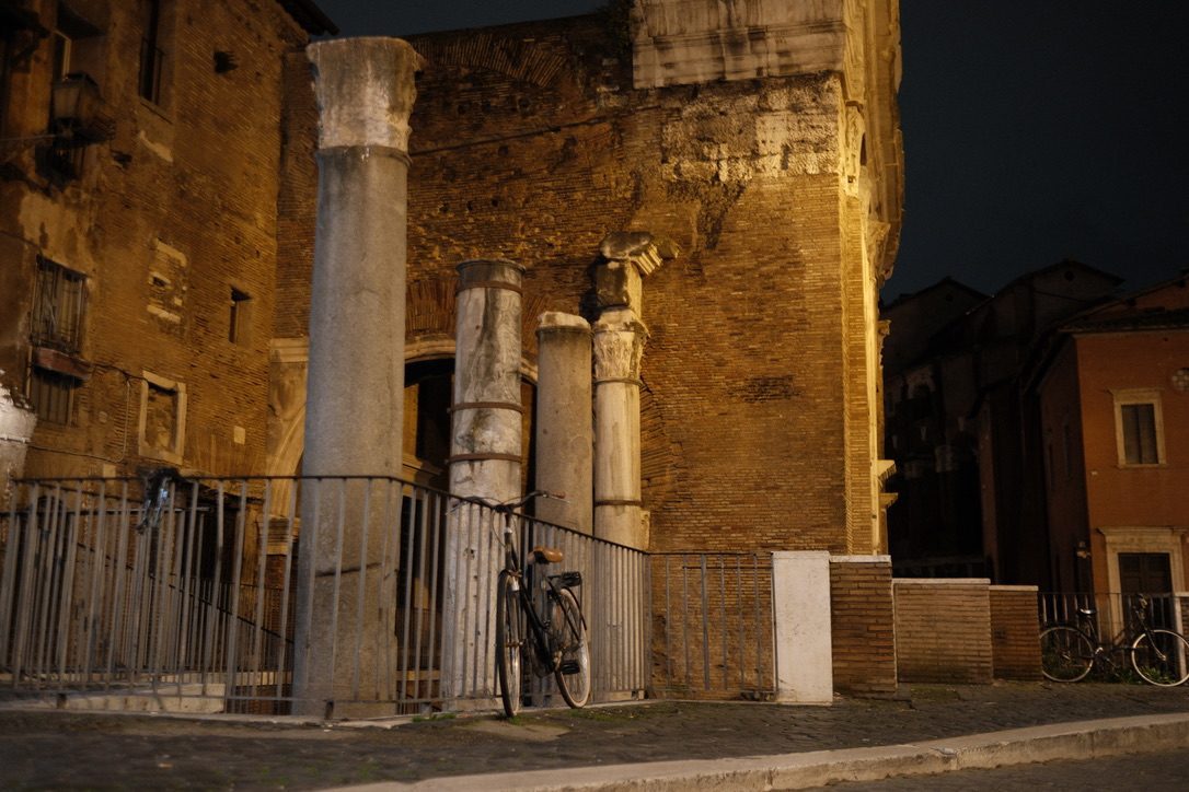 The columns of the Portico d’Ottavia at night, with a bicycle leaning on the railing